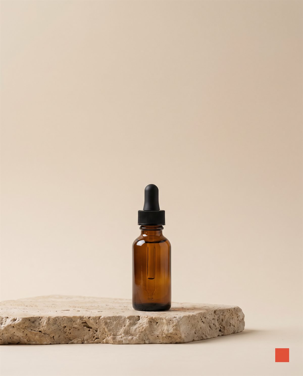 Amber glass serum dropper on a travertine plinth against a warm bone backdrop