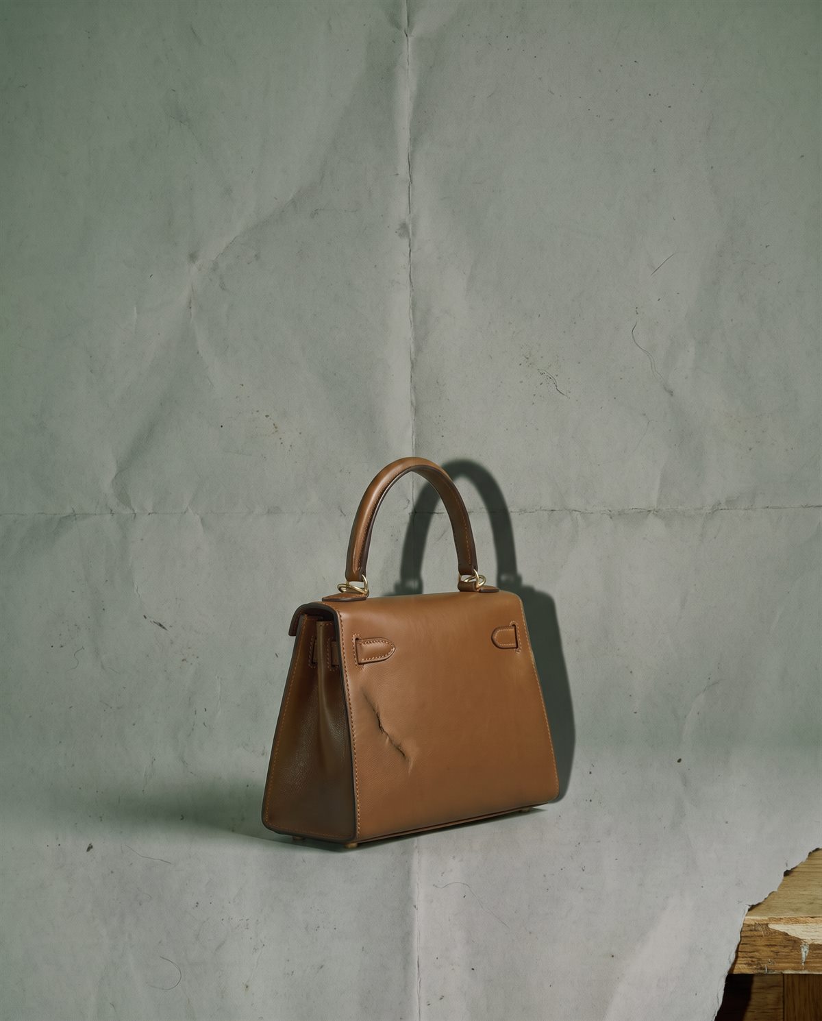 Raw capture: the same handbag on creased grey paper with flat light and dust
