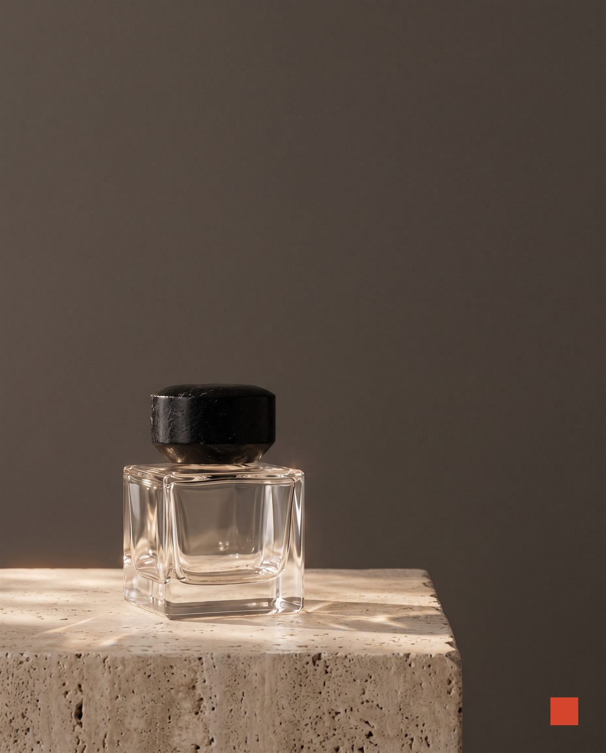 Clear glass perfume flacon with a black stone cap on a travertine pedestal