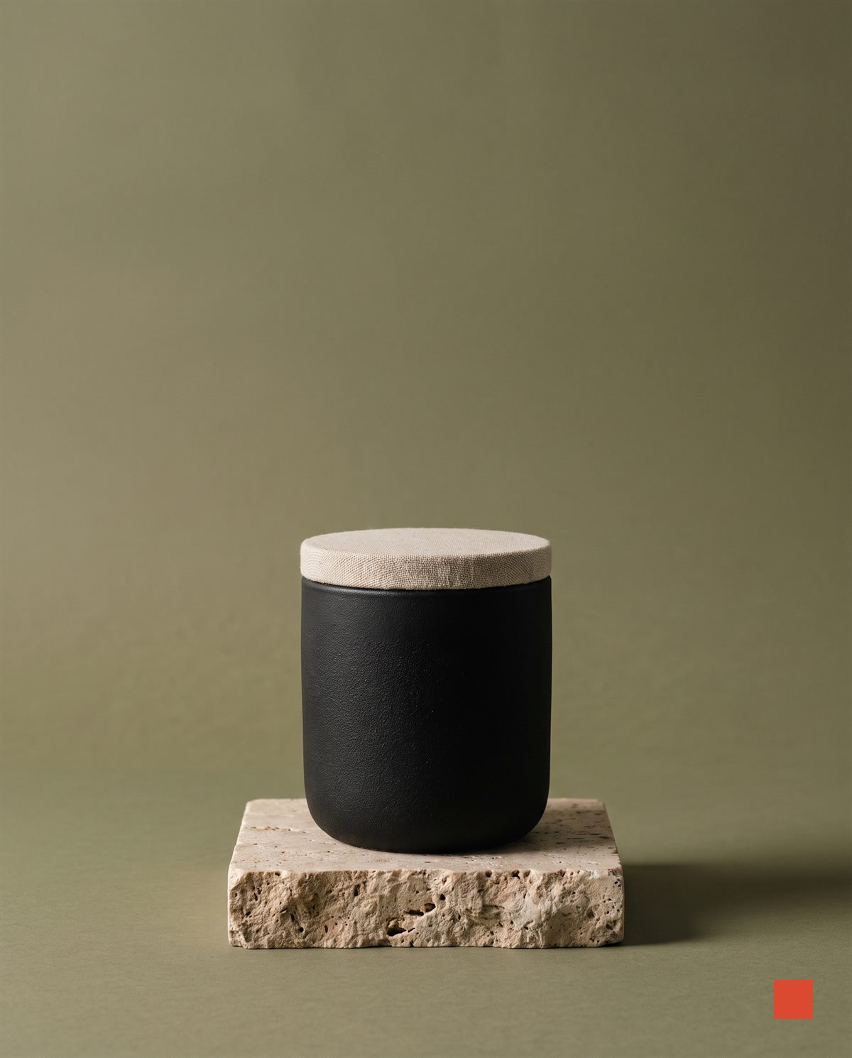 Black ceramic candle vessel on a travertine block against an olive backdrop